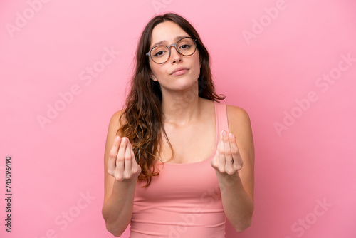 Young caucasian woman isolated on pink background making money gesture but is ruined
