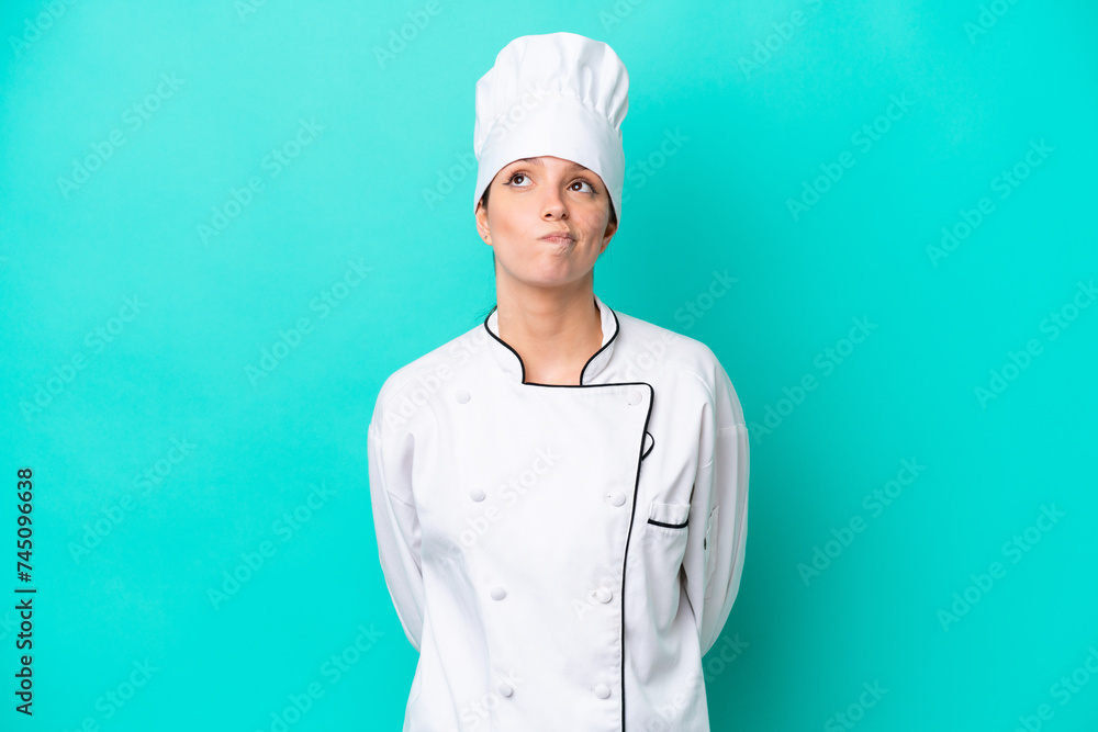 Young caucasian chef woman isolated on blue background and looking up Young caucasian chef woman isolated on blue background and looking up