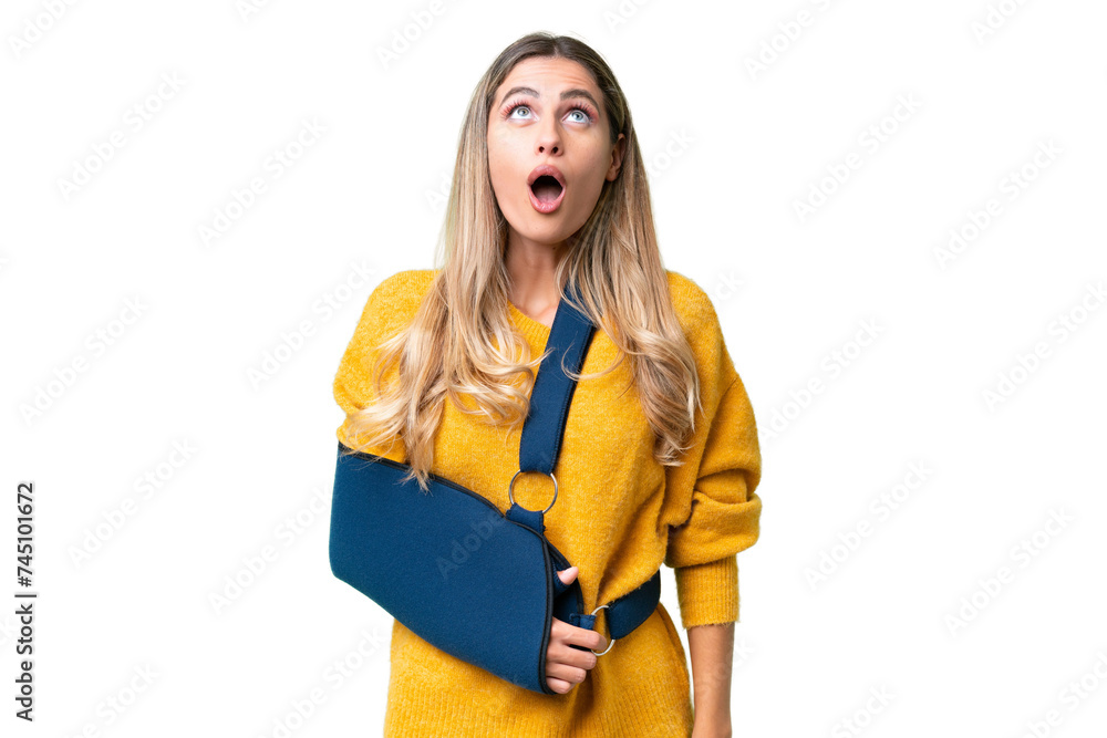 Young Uruguayan woman with broken arm and wearing a sling over isolated background looking up and with surprised expression Young Uruguayan woman with broken arm and wearing a sling over isolated background looking up and with surprised expression