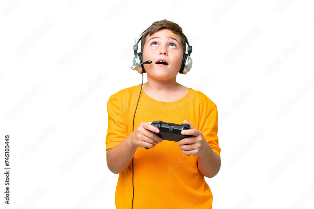 Little caucasian kid playing with a video game controller over isolated chroma key background looking up and with surprised expression