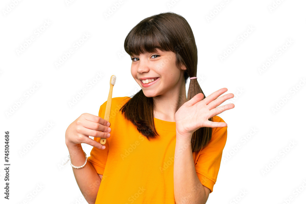 Little caucasian girl brushing teeth over isolated background saluting with hand with happy expression