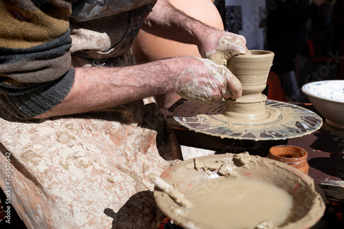 Artesano alfarero trabajando en el torno sobre una vasija de barro y arcilla. photo