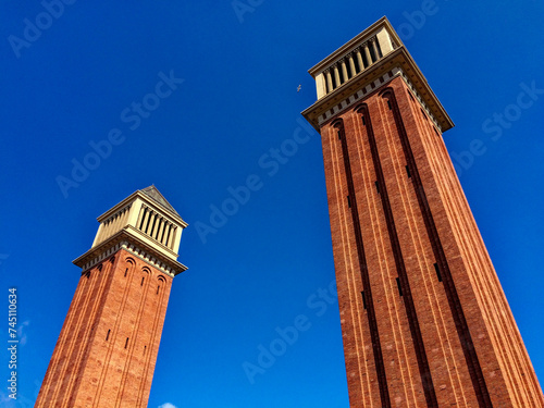 The image shows two tall red brick towers with white architectural details under a clear blue sky. photo