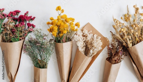 Dry flowers in bunches in brown craft paper packaging on white background. Flat lay photo