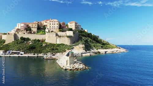 The lighthouse at the entrance to the port of the city of Calvi and its medieval fort , in Europe, France, Corsica, by the Mediterranean Sea, in summer, on a sunny day. photo