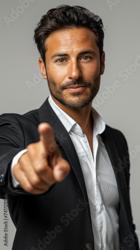 A businessman in a professional suit is pointing directly at the camera in a confident gesture.