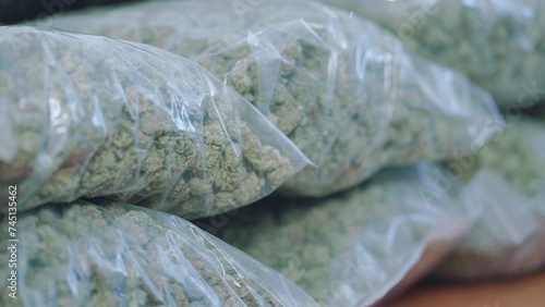 Cannabis warehouse, shot of sealed plastic bag with marijuana inside, laying on the table ready to ship out, drug narcotic trafficking, smuggling drugs, illegal substances, stack of weed flowers