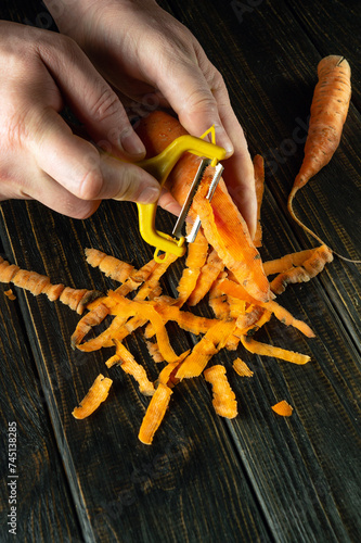 The cook hands peel carrots with a vegetable peeler on the kitchen table in a restaurant. Preparing a vegetable dish for dinner photo