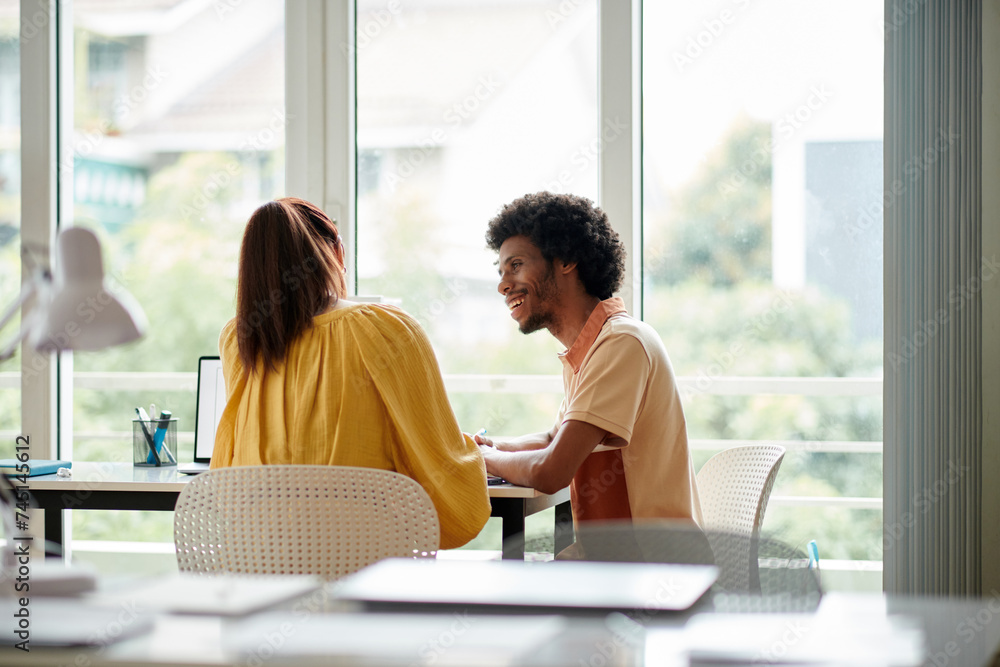 Cheerful colleagues sitting at office desk and enjoying working on project together Cheerful colleagues sitting at office desk and enjoying working on project together