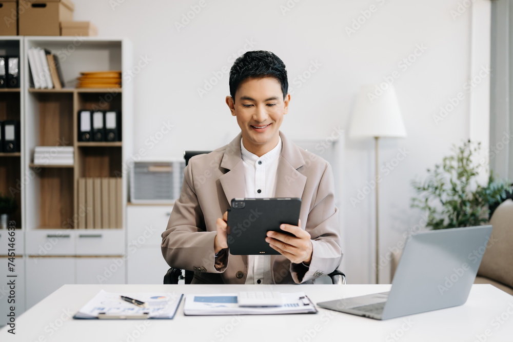 Asian businessman typing laptop and tablet Placed at the table at the office. Asian businessman typing laptop and tablet Placed at the table at the office.