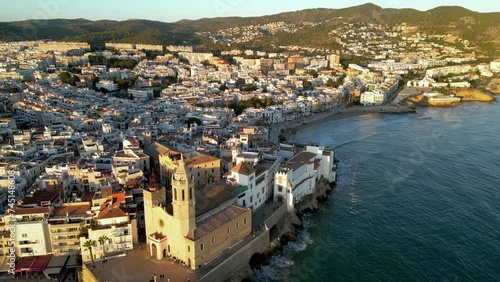 Panoramic aerial view of Sitges, Costa Dorada, Spain. Beautiful sunset colours reflecting on the building and beach. Famous travel destination. Golden hour point. Static footage.