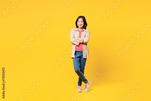 Full body fun young woman of Asian ethnicity she wear pink t-shirt beige shirt pastel casual clothes hold hands crossed folded isolated on plain yellow background studio portrait. Lifestyle portrait.