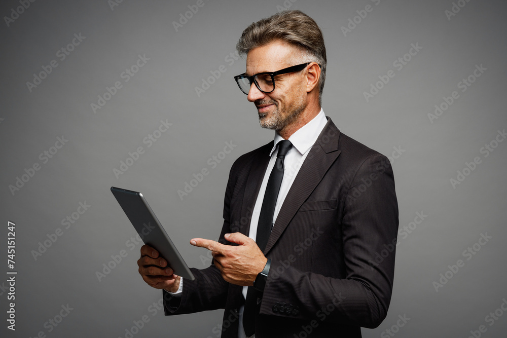 Adult successful employee business man corporate lawyer wear classic formal black suit shirt tie work in office hold use digital tablet pc computer isolated on plain grey background studio portrait.