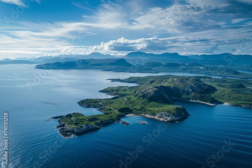 A breathtaking aerial view of a green island amidst the vast blue ocean under a cloudy sky.