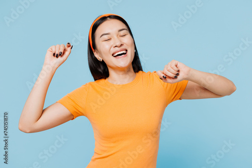 Young vivid vibe happy woman of Asian ethnicity wear orange t-shirt casual clothes raise up hands dance have fun isolated on plain pastel light blue cyan background studio portrait. Lifestyle concept.