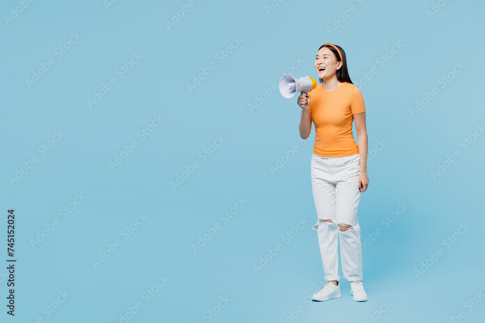 Full body young woman of Asian ethnicity wear orange t-shirt casual clothes hold in hand megaphone scream announces discounts sale Hurry up isolated on plain blue cyan background. Lifestyle concept. Full body young woman of Asian ethnicity wear orange t-shirt casual clothes hold in hand megaphone scream announces discounts sale Hurry up isolated on plain blue cyan background. Lifestyle concept.