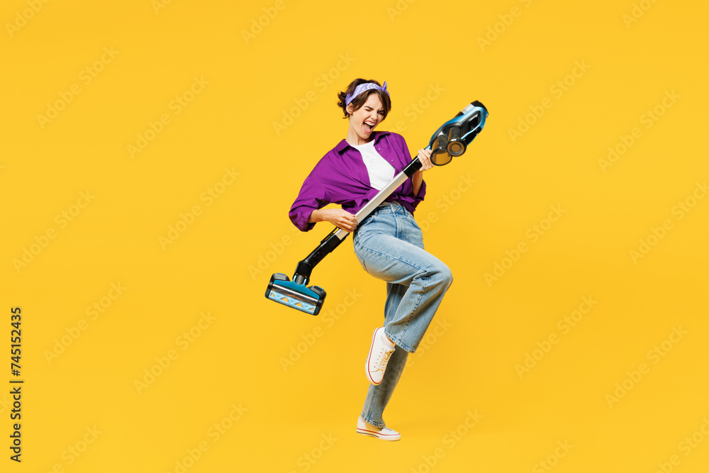 Full body side view young woman wearing purple shirt casual clothes do housework tidy up hold vacuum cleaner pov play guitar isolated on plain yellow background studio portrait. Housekeeping concept. Full body side view young woman wearing purple shirt casual clothes do housework tidy up hold vacuum cleaner pov play guitar isolated on plain yellow background studio portrait. Housekeeping concept.