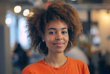 woman with a radiant smile and a natural afro hairstyle poses confidently in a vibrant orange shirt