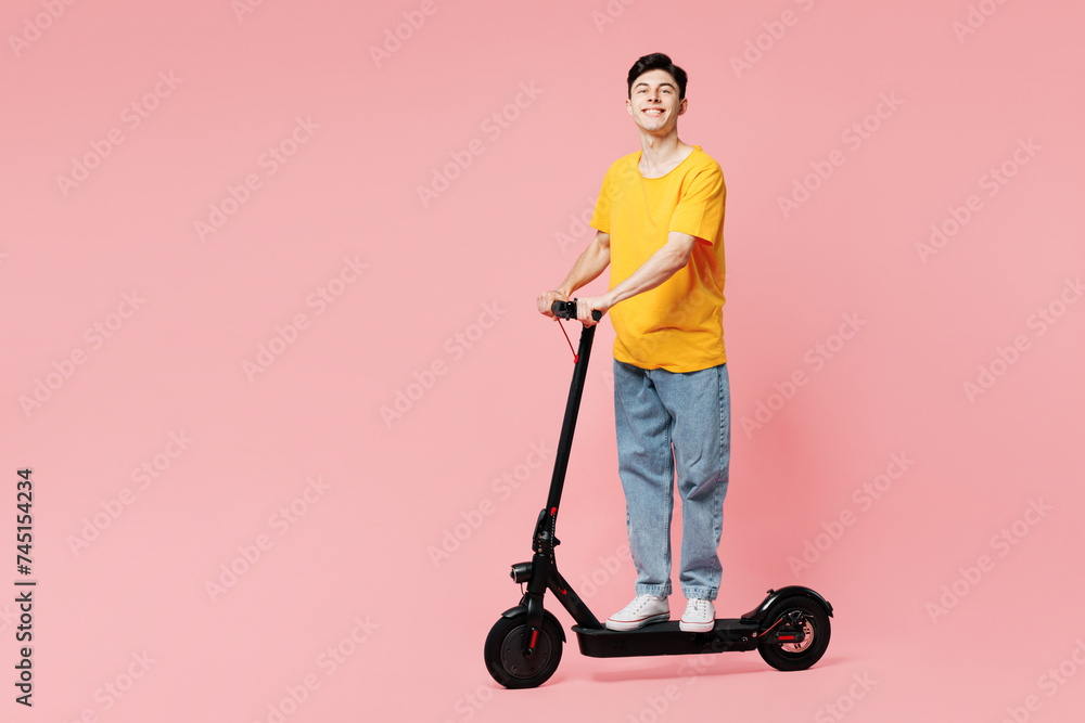 Full body side profile view smiling happy young man he wears yellow t-shirt casual clothes driving electric scooter isolated on plain pastel light pink background studio portrait. Lifestyle concept. Full body side profile view smiling happy young man he wears yellow t-shirt casual clothes driving electric scooter isolated on plain pastel light pink background studio portrait. Lifestyle concept.