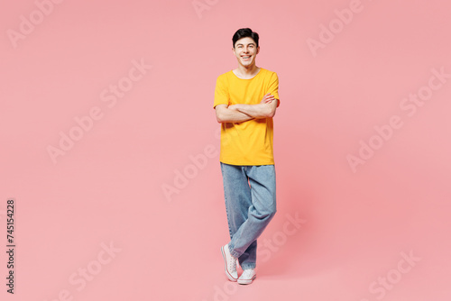 Full body smiling happy cheerful young man wears yellow t-shirt casual clothes hold hands crossed folded look camera isolated on plain pastel light pink background studio portrait. Lifestyle concept