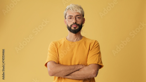 Guy with glasses, dressed in yellow T-shirt, crossing arms and looking at camera isolated on yellow background in studio