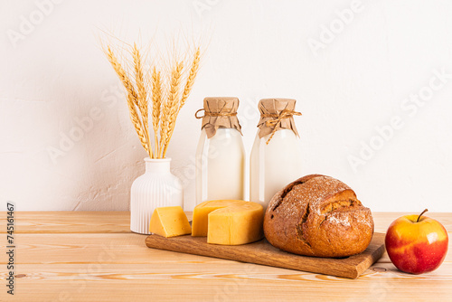 A variety of fresh dairy products, bread, ears of corn, apples on a wooden table. Treats and symbols of the Jewish holiday of Shavuot