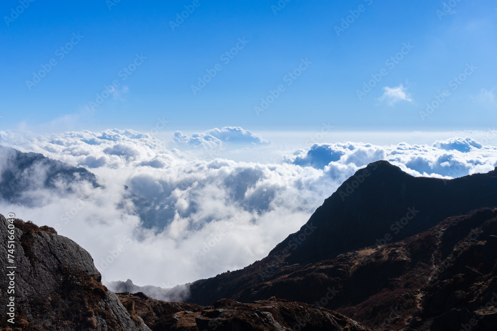 A mesmerizing high-point view of clouds from the mountaintop. Silver-white clouds filled in the valley surrounded by rocky brown mountains amid a clear blue sky are the best place to meditate. Sikkim,