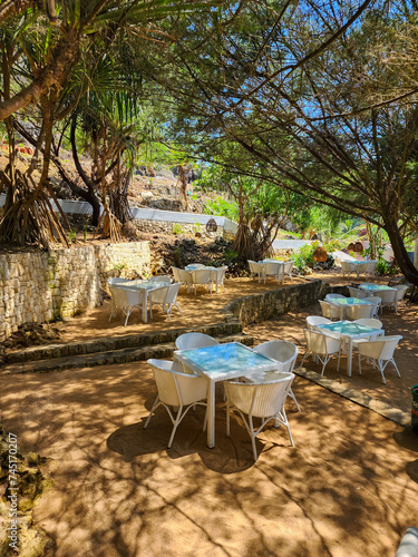 White plastic chairs and tables in an outdoor or outside sitting garden under the trees on a sunny day