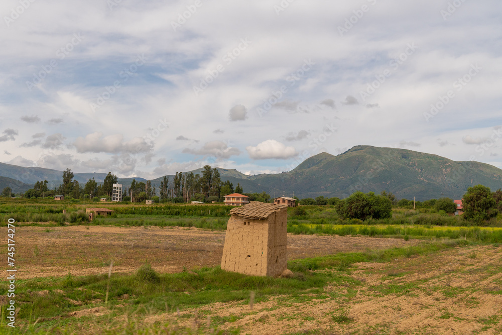 Obraz premium rural house in a green cultivated meadow, farm in a beautiful cultivated valley with mountains in the background