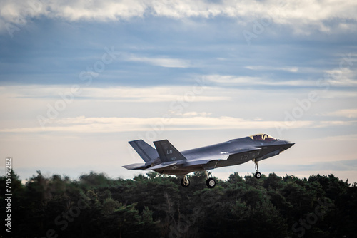 F35 coming into land at RAF Lakenheath with landing gear down, images shows the fighter jet coming into land with a cloudy sky and trees photo