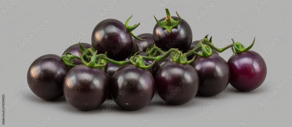 A group of black tomatoes, including Brads Atomic Grape heirloom cultivars of Solanum lycopersicum, are arranged on a plain gray background. The tomatoes vary in size, shape, and texture, creating a A group of black tomatoes, including Brads Atomic Grape heirloom cultivars of Solanum lycopersicum, are arranged on a plain gray background. The tomatoes vary in size, shape, and texture, creating a