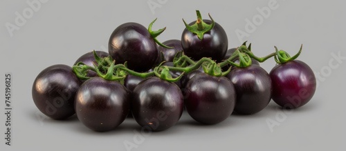 A group of black tomatoes, including Brads Atomic Grape heirloom cultivars of Solanum lycopersicum, are arranged on a plain gray background. The tomatoes vary in size, shape, and texture, creating a photo