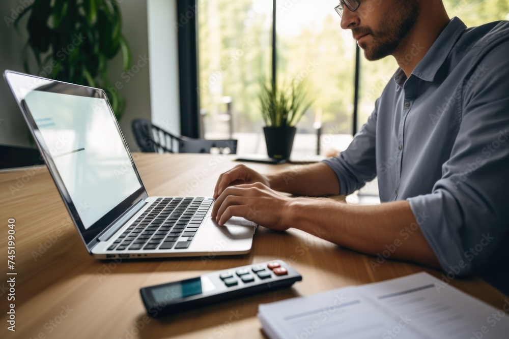 A man sitting at a table with a laptop and calculator. Suitable for business and finance concepts A man sitting at a table with a laptop and calculator. Suitable for business and finance concepts