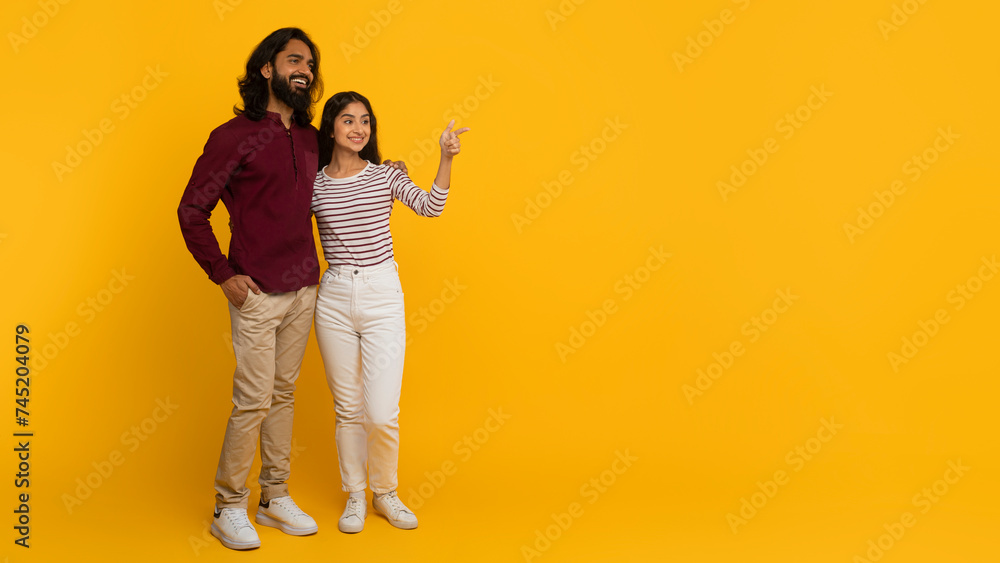 Positive millennial indian couple pointing at copy space Positive millennial indian couple pointing at copy space
