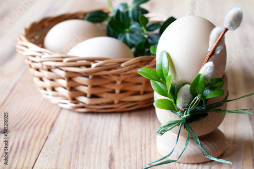 Egg in egg cup decorated catkins and boxwood and eggs in basket on wooden background, easter concept 