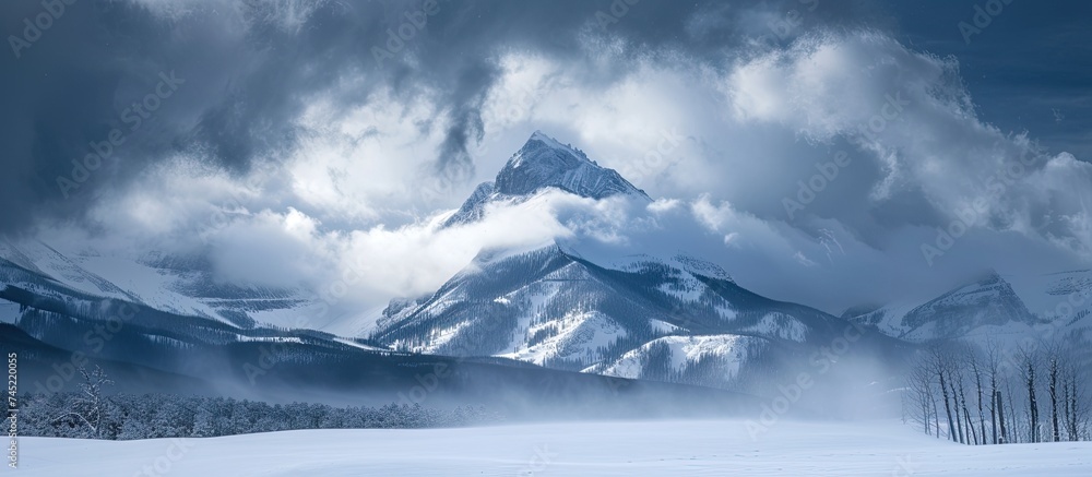 A grand mountain rises above a snow-covered landscape, with its peak and slopes blanketed in pristine white snow. The scene is enhanced by the dramatic backdrop of thick, heavy clouds hovering above.