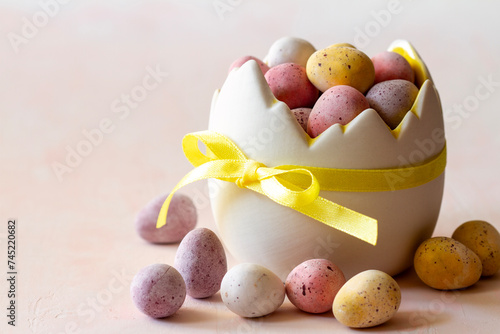 Colored chocolate easter eggs candy in eggshell shaped bowl on pink background, easter sweets, decoration