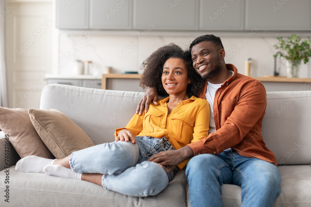 Black young millennial couple find relaxation on couch embracing indoor