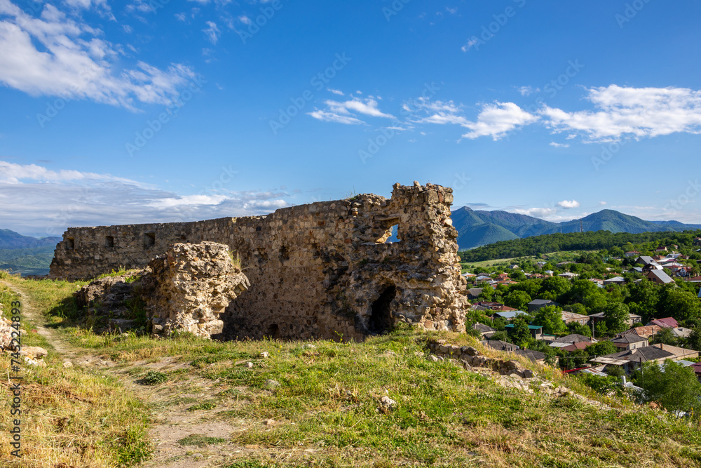 Surami fortress grass courtyard with ruins of stone defense wall, Surami village landscape with Likhi mountain range in the background.