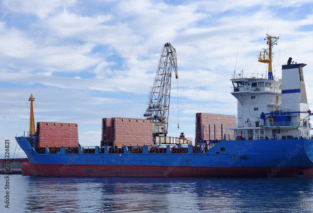 Cargo ship in port ready for load or unload against the blue sky with some white clouds