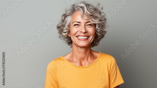 Close up of  mature woman with white skin, grey short hair, wavy hair and a clear yellow t shirt, isolated in a light grey studio. Portrait person. photo