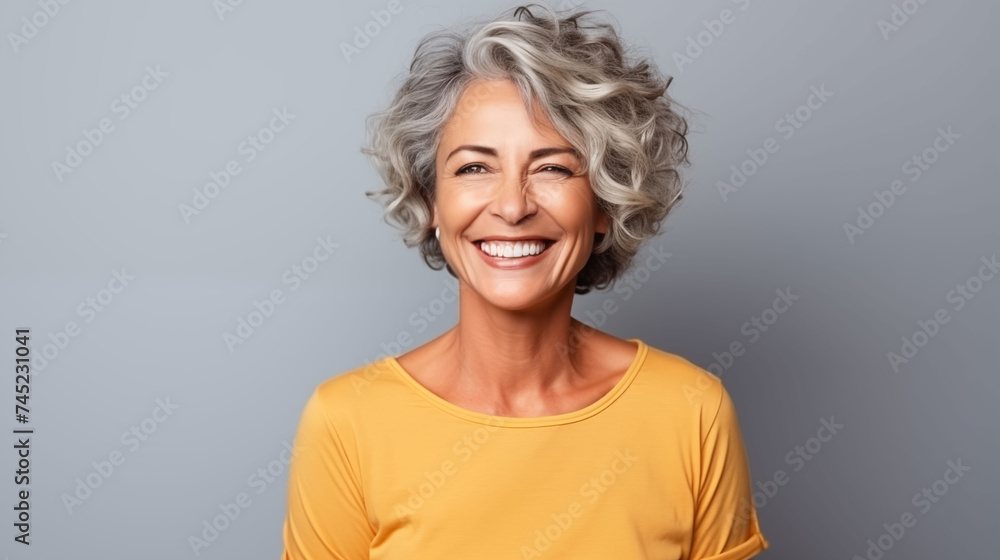 Close up of  mature woman with white skin, grey short hair, wavy hair and a clear yellow t shirt, isolated in a light grey studio. Portrait person. - obrazy, fototapety, plakaty 