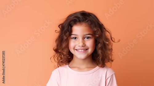 Close up of girl with brown skin, brown long hair, wavy hair and a clear pink t shirt, isolated in a light orange studio. Portrait person.