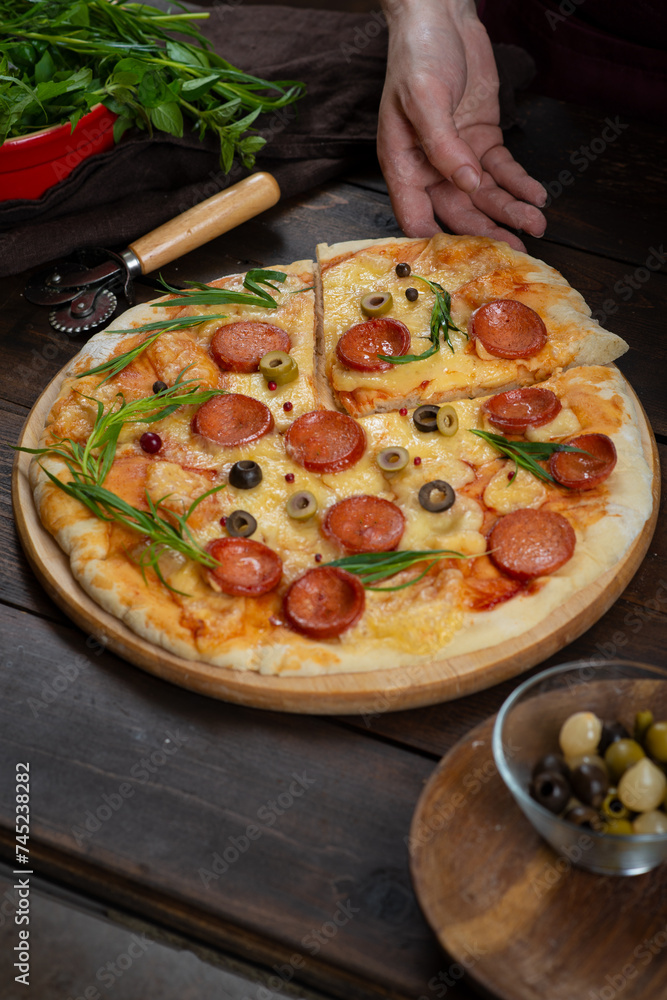 Homemade pizza with pepperoni, cheese and herbs on a dark wooden background