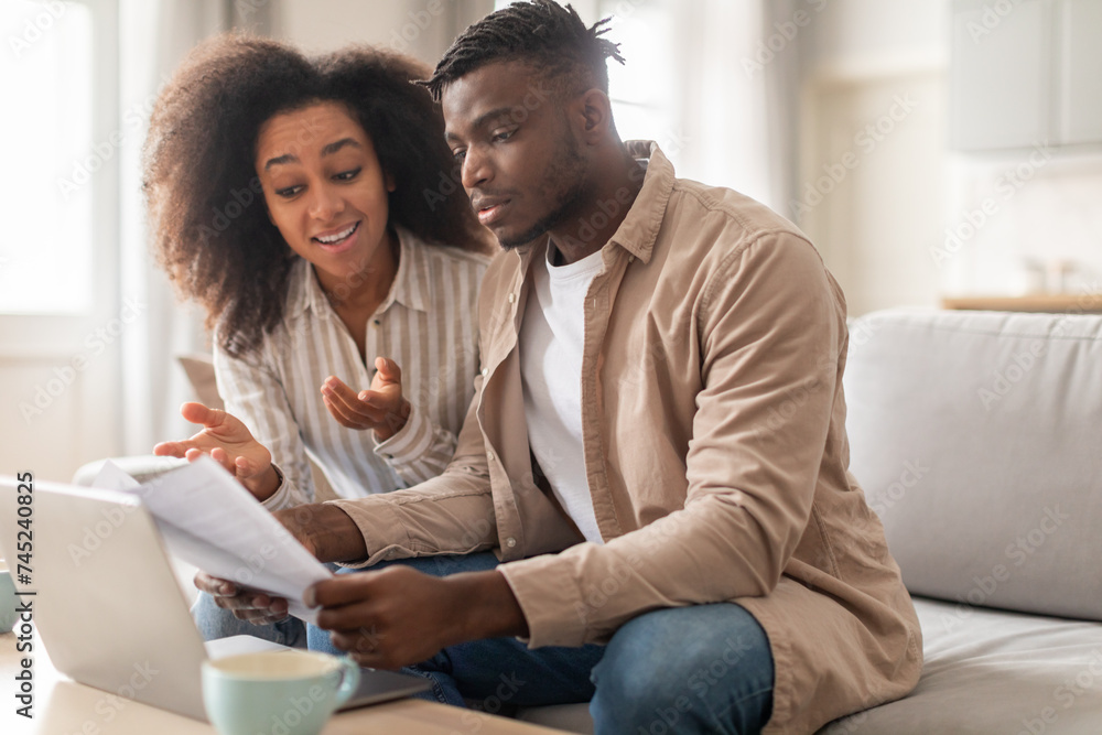 Obraz premium Young African American spouses handling paperwork sitting near laptop indoor