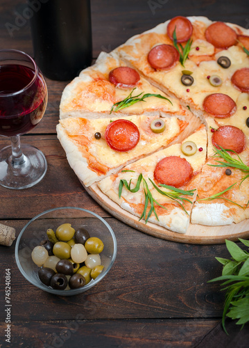 Homemade pizza with pepperoni, cheese and herbs on a dark wooden background