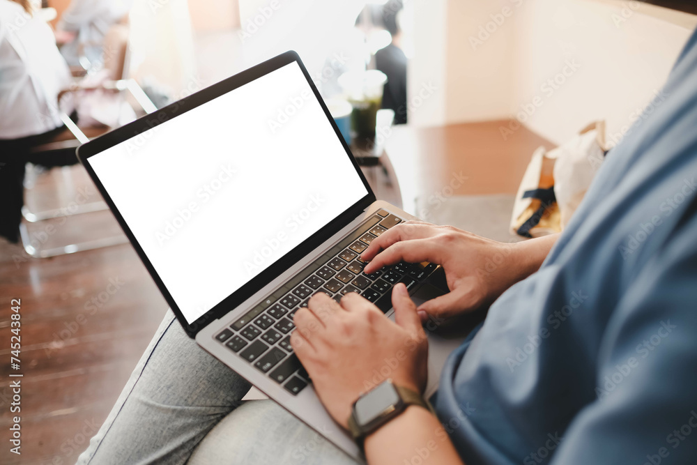 Mockup image of laptop computer. A man sitting cross legged with laptop computer with blank white screen at coffee cup, over shoulder view Mockup image of laptop computer. A man sitting cross legged with laptop computer with blank white screen at coffee cup, over shoulder view