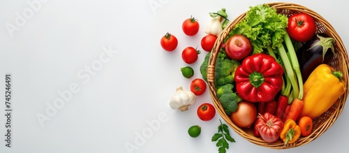 A top-down view of a basket brimming with various types of fresh, colorful vegetables on a white background. The assortment includes carrots, tomatoes, bell peppers, cucumbers, and more. © TheWaterMeloonProjec