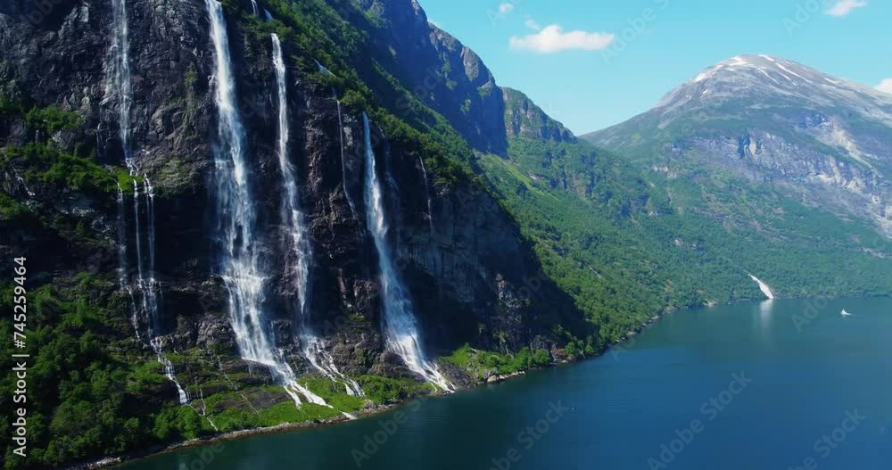 Breathtaking aerial footage of the Seven Sisters waterfall in Norway's Geirangerfjord. A vibrant rainbow arcs over the cascading waters on a sunny day, showcasing the stunning natural beauty. Travel 