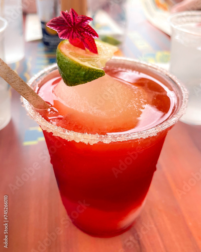 Obraz na płótnie Frozen strawberry daiquiri sitting on table, with its rim salted and a vibrant lime wedge adds a zesty pop of color. Completing the picturesque scene is a tropical flower resting on top the drink. w salonie